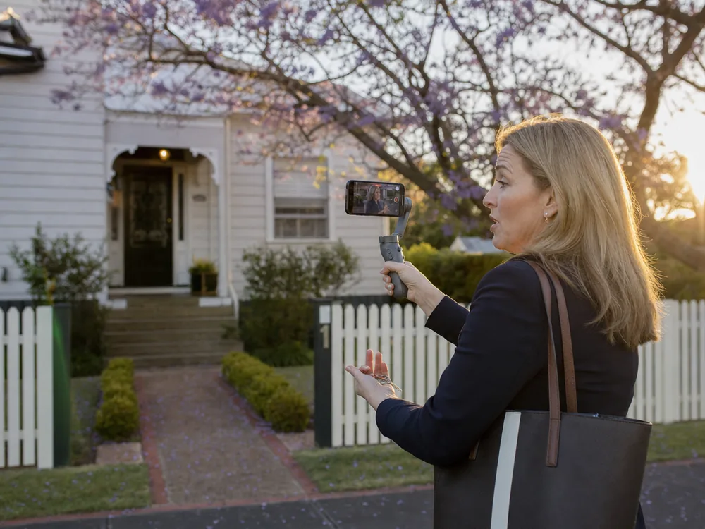 Agent filming a piece to camera on her phone outside a listing